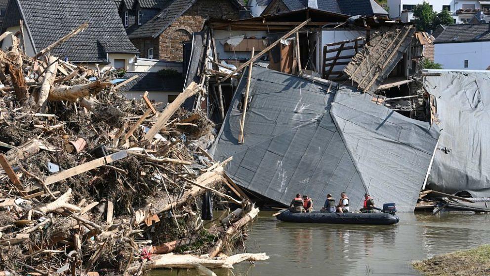 Military personnel floats on a boat on the Ahr river as the roof of a damaged house hangs on the water and uprooted trees are
